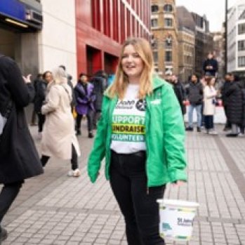 St John Ambulance volunteer standing in a busy street carrying a plastic collection bucket.